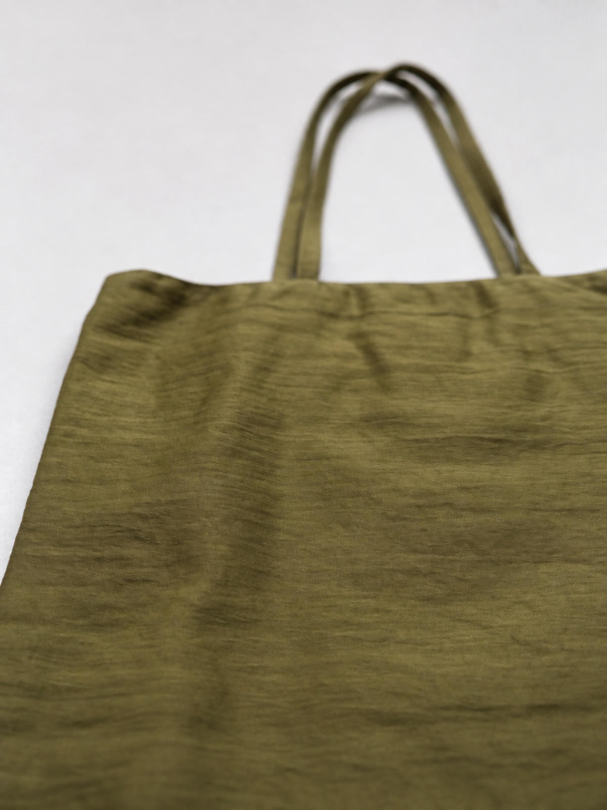 An olive green fabric tote bag with two shoulder straps, shown against a plain light background.