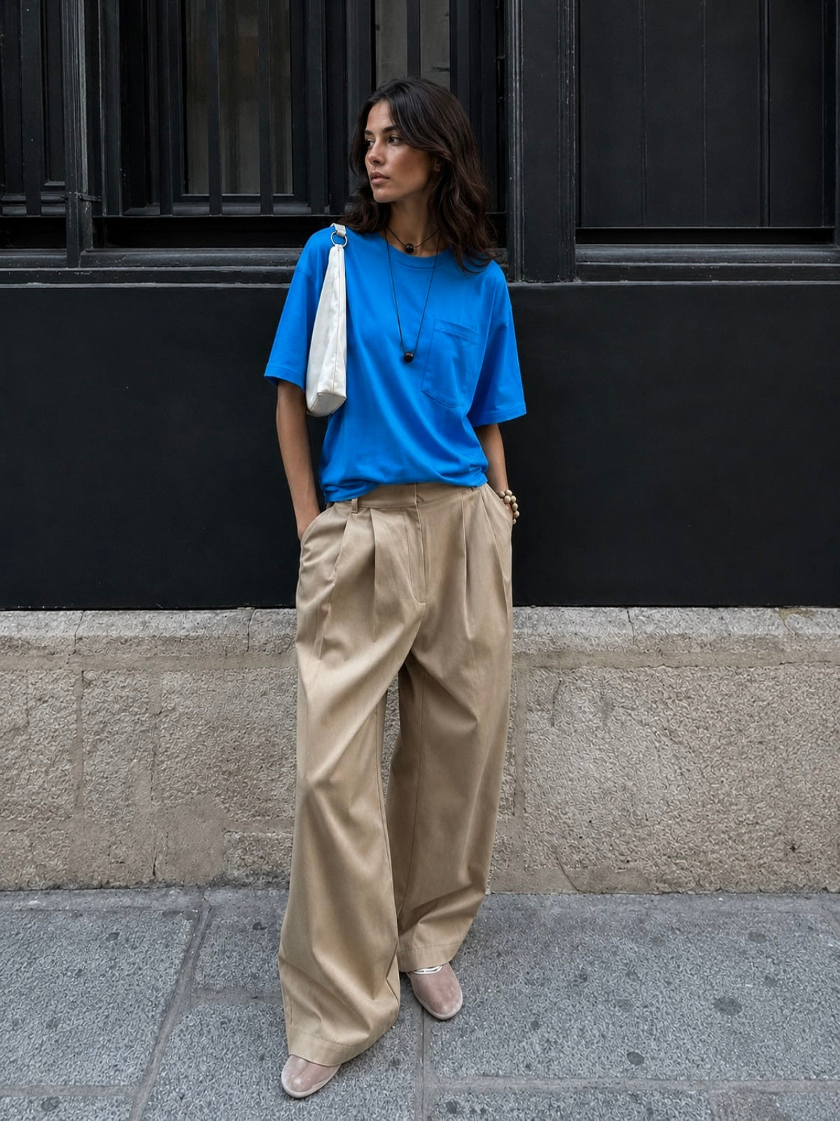 Woman wearing a blue shirt and beige pants standing against a black building.