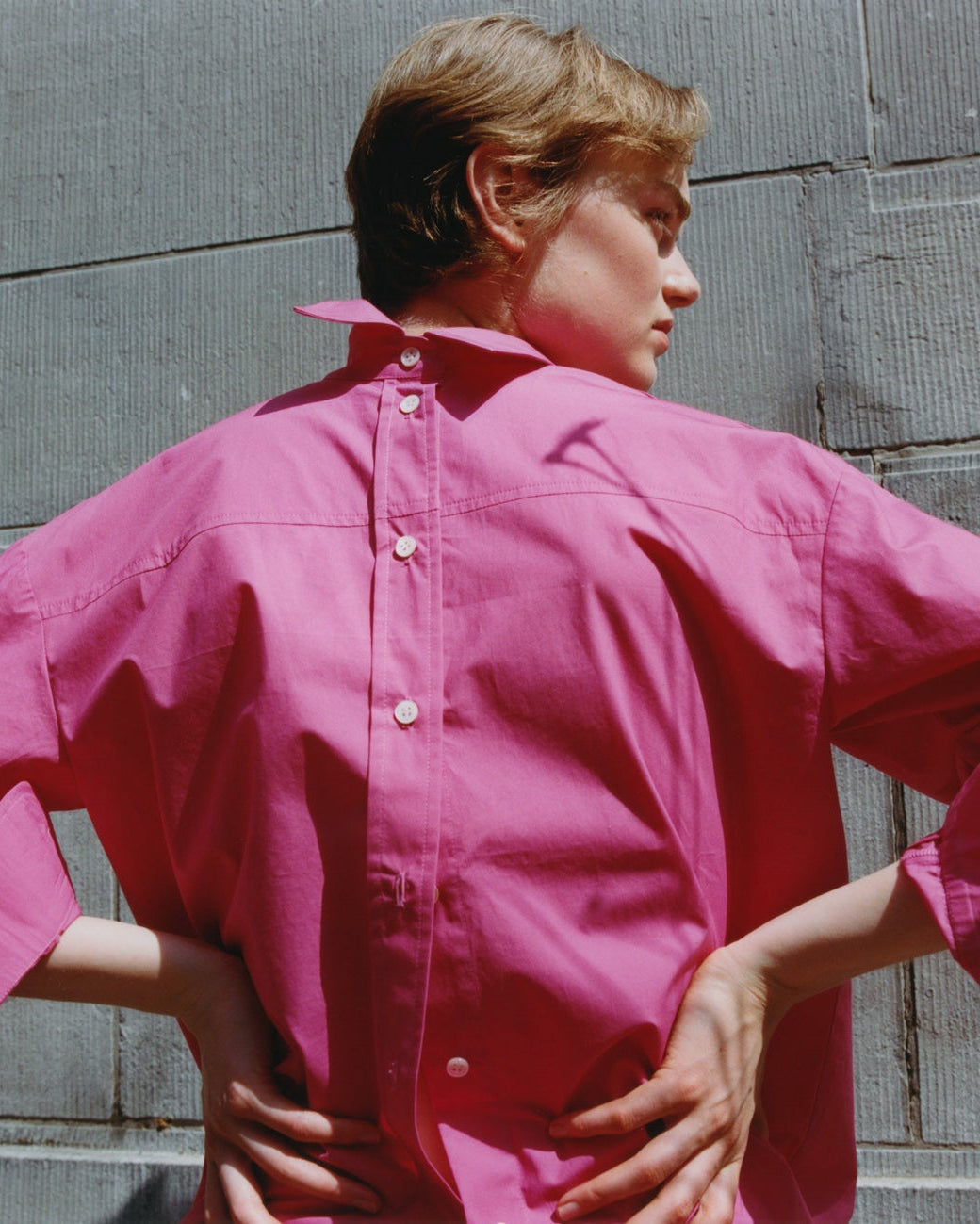 Person wearing a pink shirt standing against a gray wall