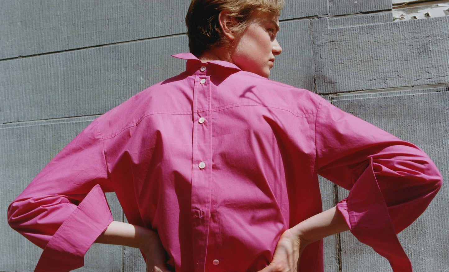 Person wearing a pink shirt standing against a gray wall